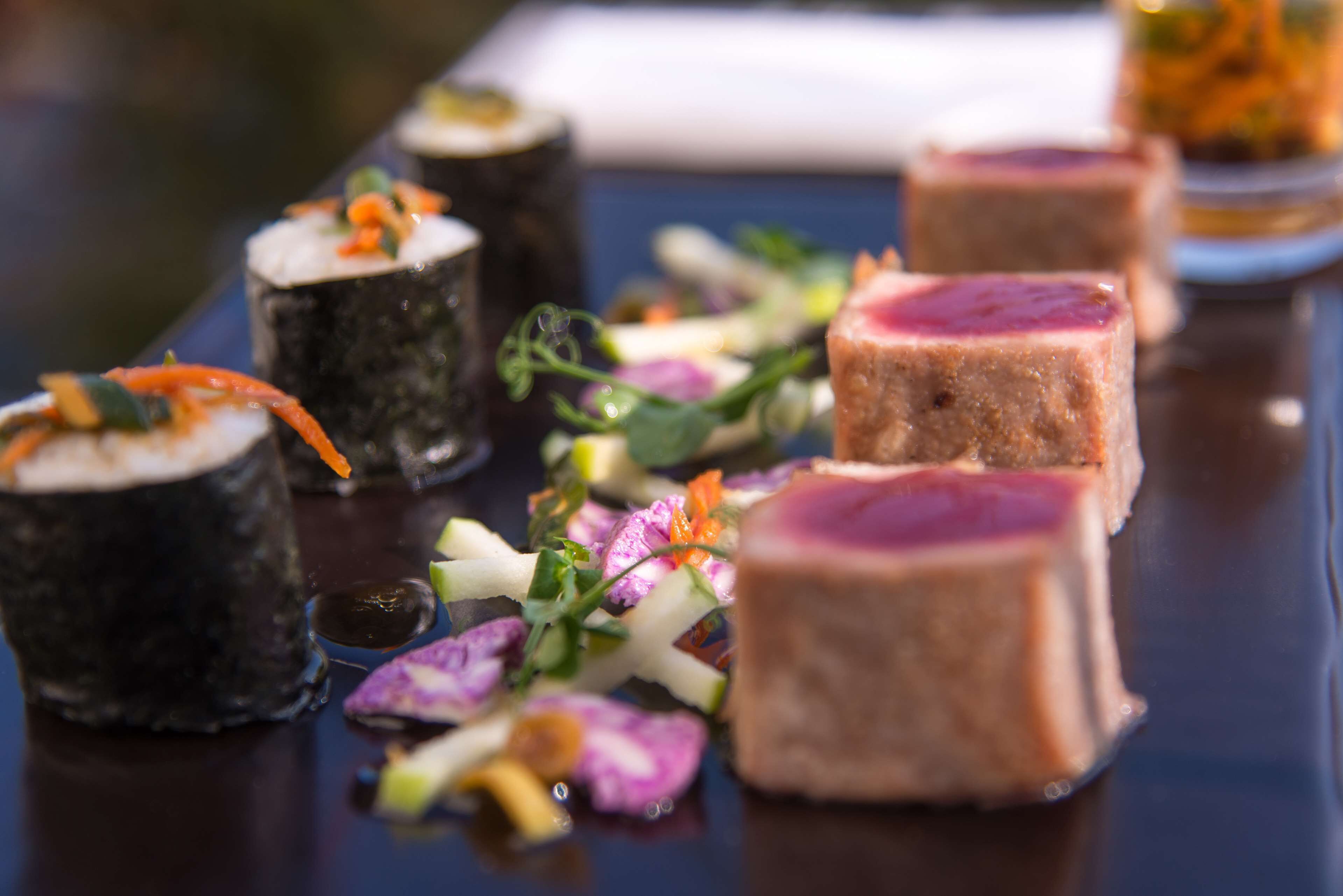 A variety of sushi and meat dishes on a dark, reflective surface.
