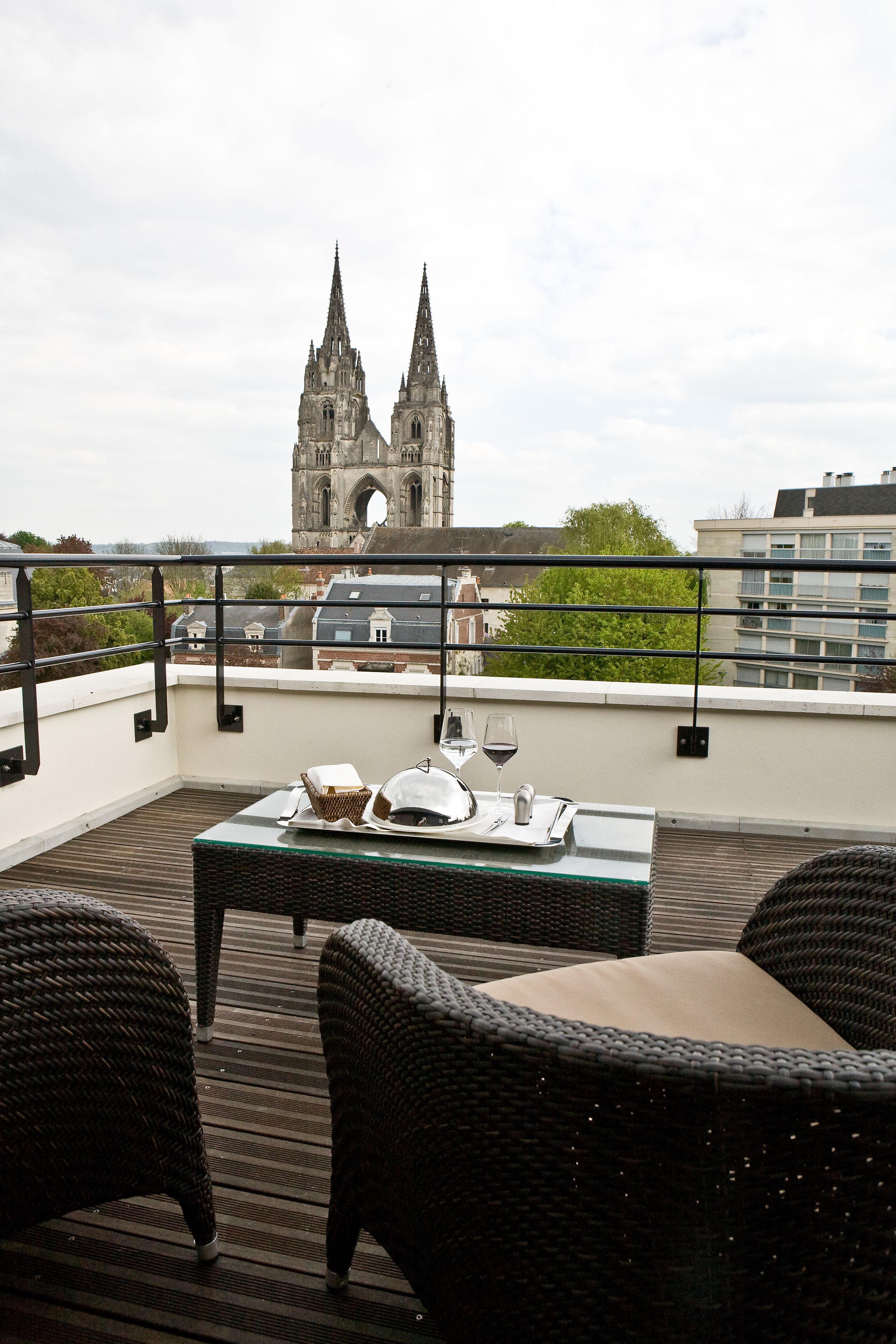 A terrace with wicker furniture, a table set with a wine glass, and a view of a cathedral in the background.