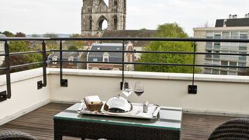 A terrace with wicker furniture, a table set with a wine glass, and a view of a cathedral in the background.