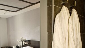 Een hotelkamer met een bed, nachtkastje en een badjas hangend aan de muur.
