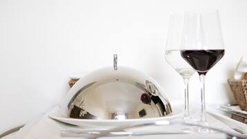 Una mesa de comedor con mantel blanco, una campana de plata, una copa de vino con vino tinto y un tenedor de plata.