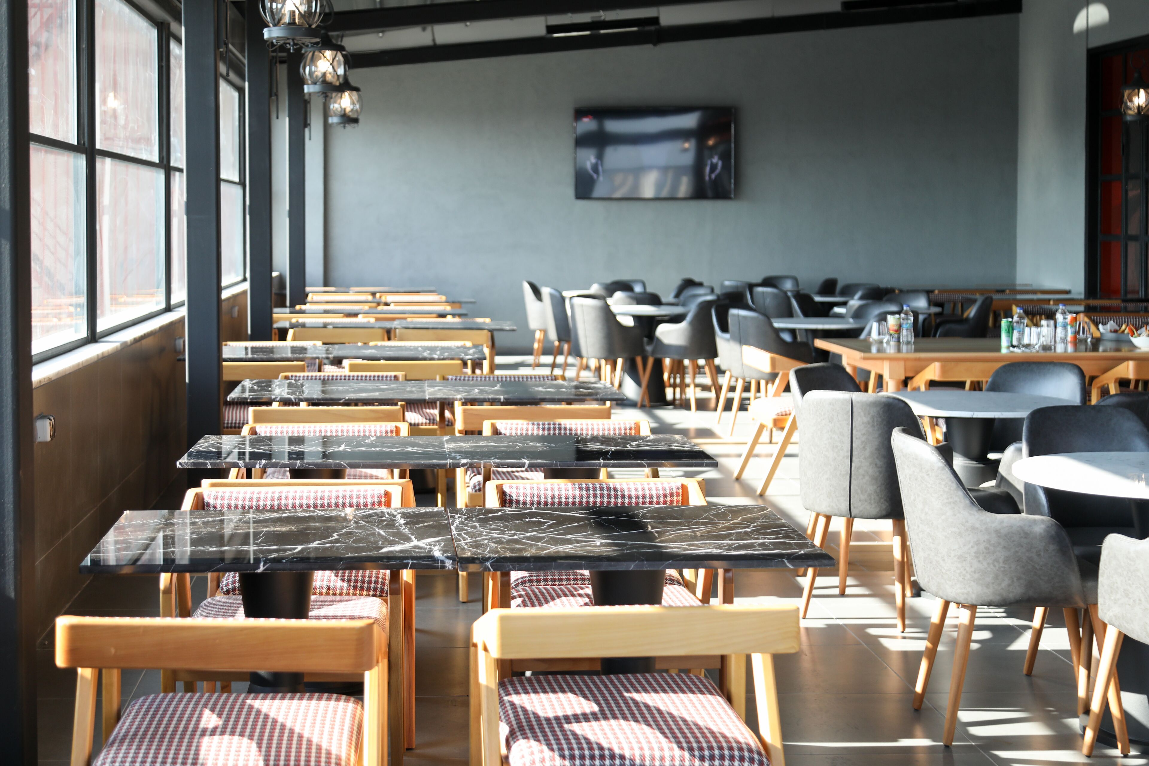 Un restaurante con varias mesas y sillas, amplias ventanas y un televisor de pantalla plana en la pared.