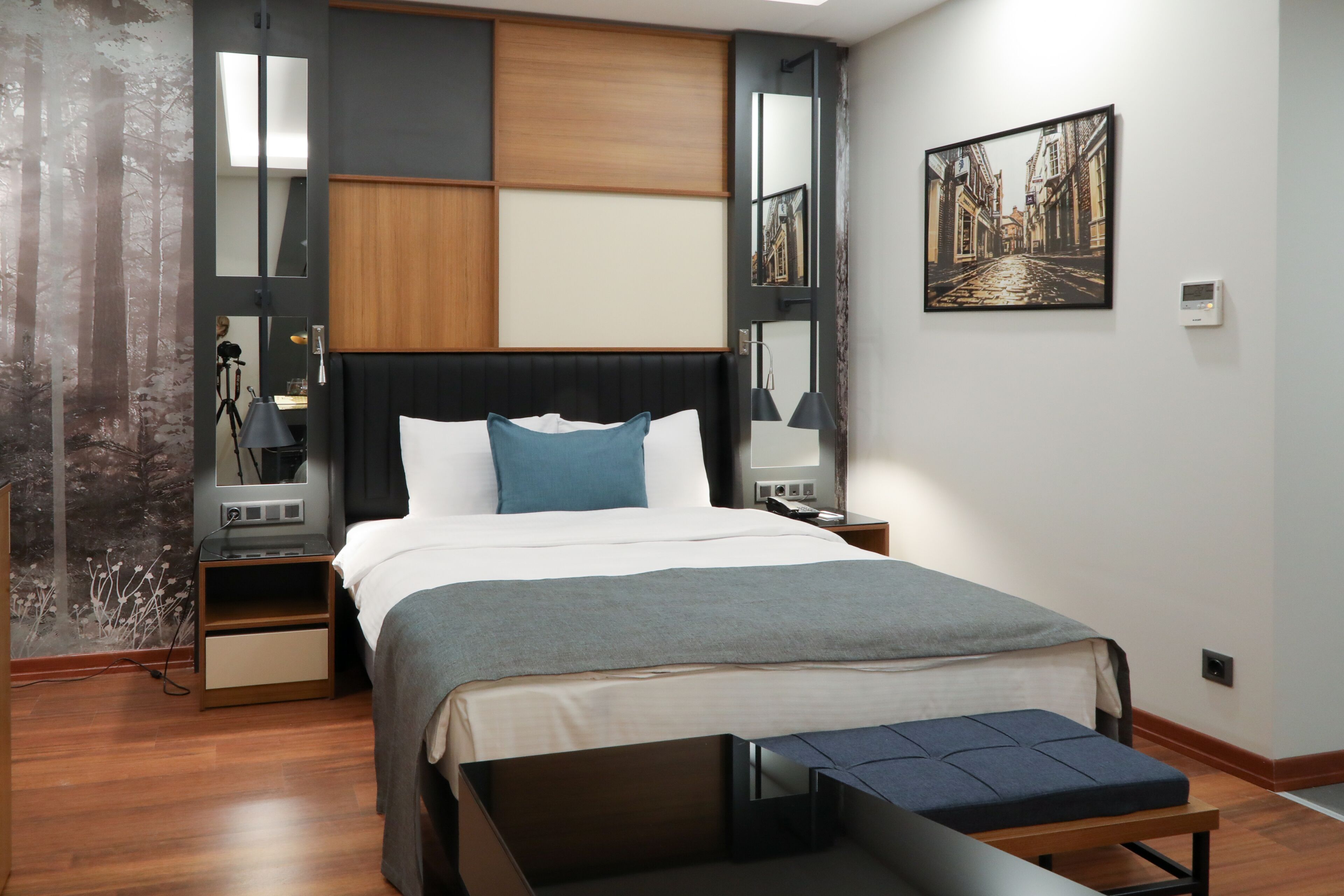 Habitación de hotel moderna con una cama grande, una mesita de noche, un banco, un televisor montado en la pared y un cuadro.