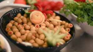 Un cuenco de aceitunas adornado con pimientos rojos y un detalle decorativo.