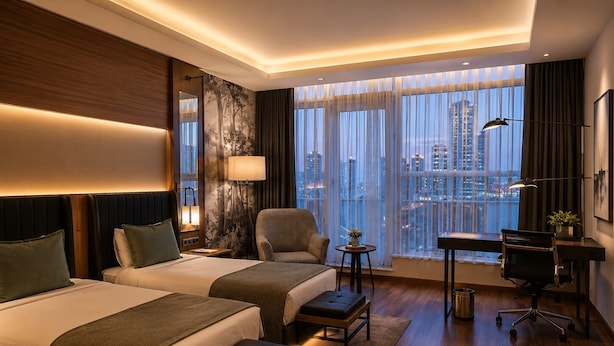Habitación de hotel con dos camas, un escritorio, una silla, una lámpara y vistas a la ciudad.