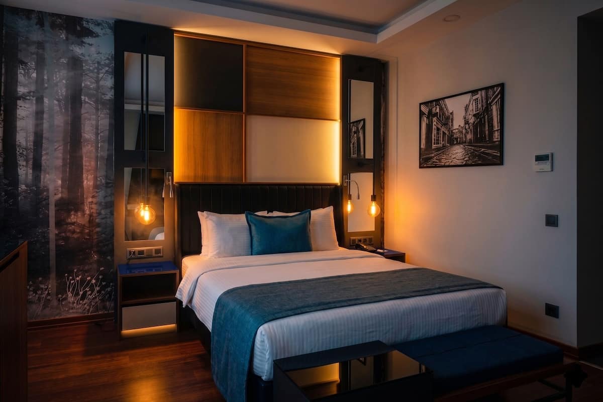 Un dormitorio moderno con una cama grande, mesitas de noche, un banco y un espejo fijado a la pared.
