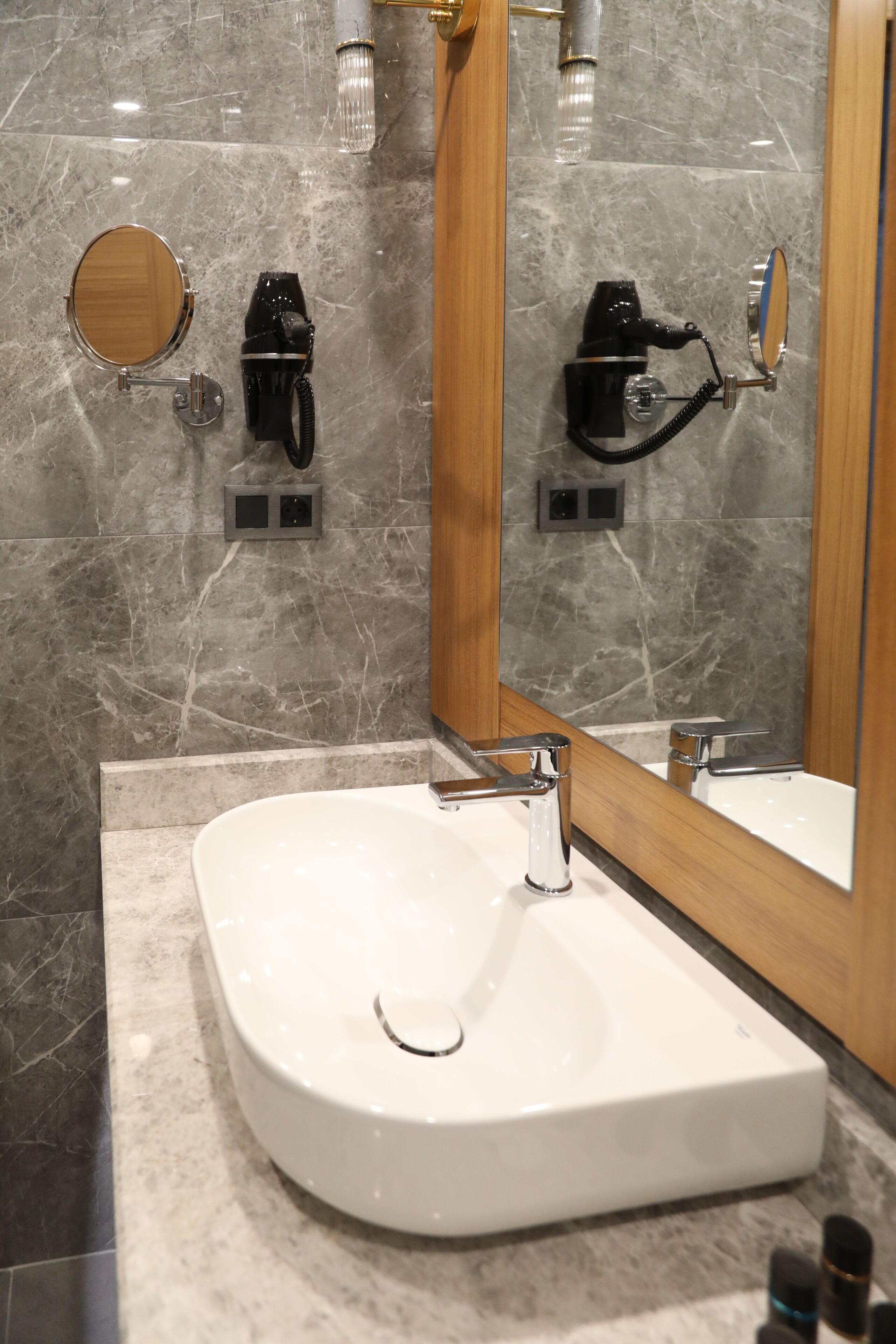 Un baño con lavamanos blanco, espejo y secador de pelo montado en la pared.