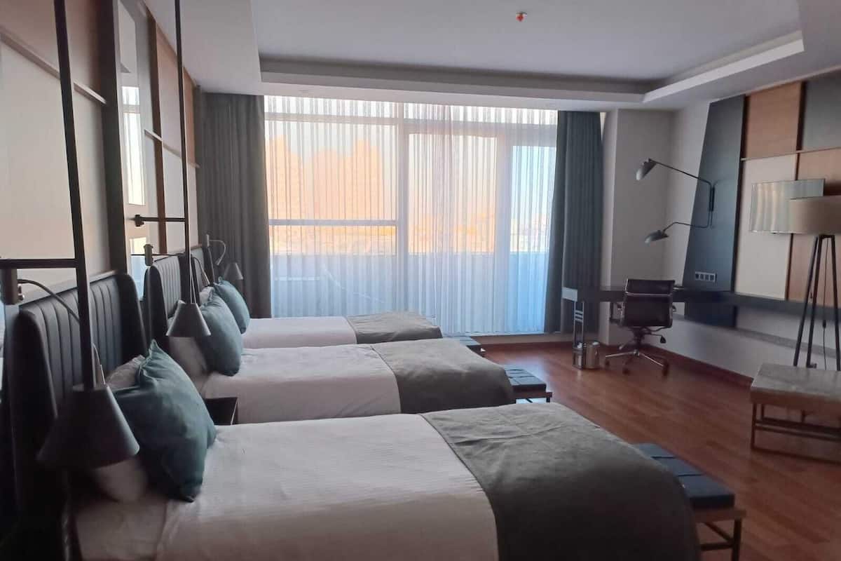 Habitación de hotel con dos camas, un escritorio, una silla y un amplio ventanal con cortinas.