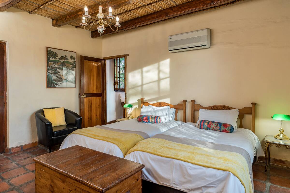 Una habitación con dos camas, una mesa de madera, una silla, una lámpara y un cuadro en la pared.