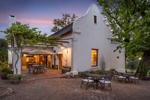 A white building with a brick patio, outdoor seating, and a well-lit entrance. - Oude Wellington (Wellington)