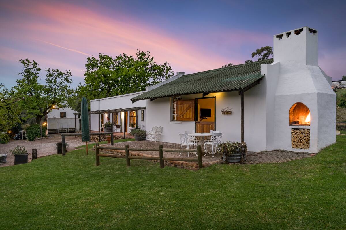 Un edificio blanco con chimenea, mesas al aire libre y un patio empedrado.