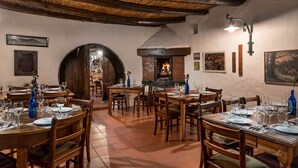 Un comedor rústico con mesas y sillas de madera, una chimenea de ladrillo y obras de arte enmarcadas en las paredes.