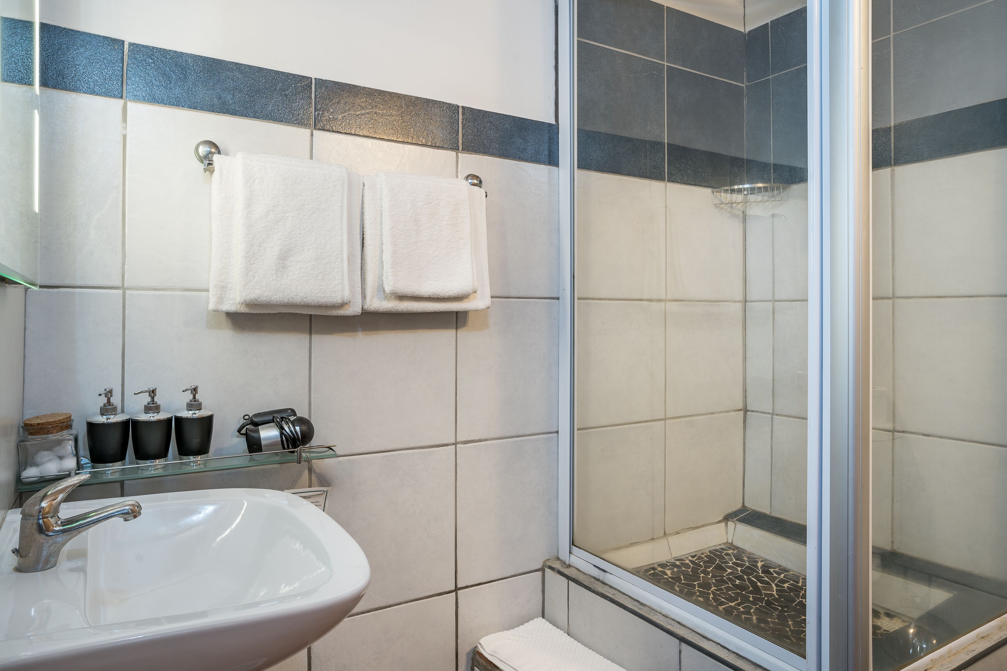 Une salle de bain avec un lavabo blanc, deux serviettes suspendues à un porte-serviettes et une douche dotée d’une porte en verre.