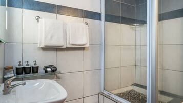 Une salle de bain avec un lavabo blanc, deux serviettes suspendues à un porte-serviettes et une douche dotée d’une porte en verre.