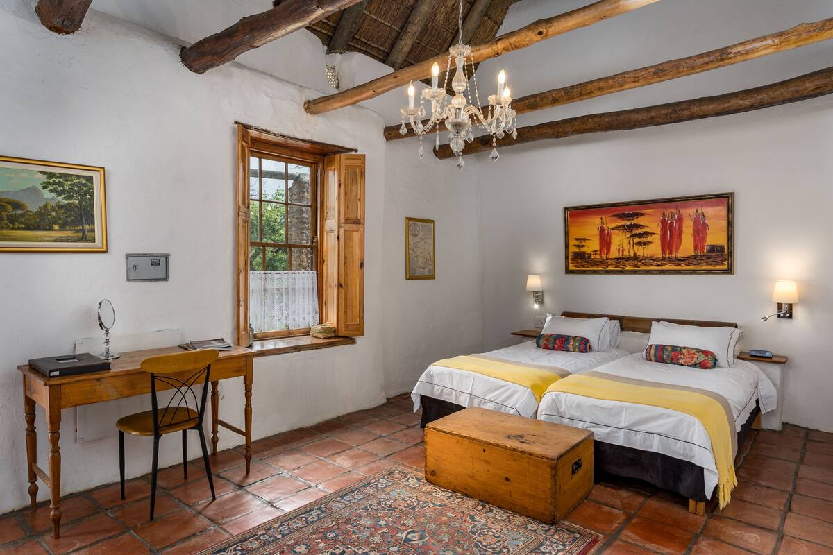 Un dormitorio con dos camas, un escritorio de madera, una silla, un ventanal y una araña.