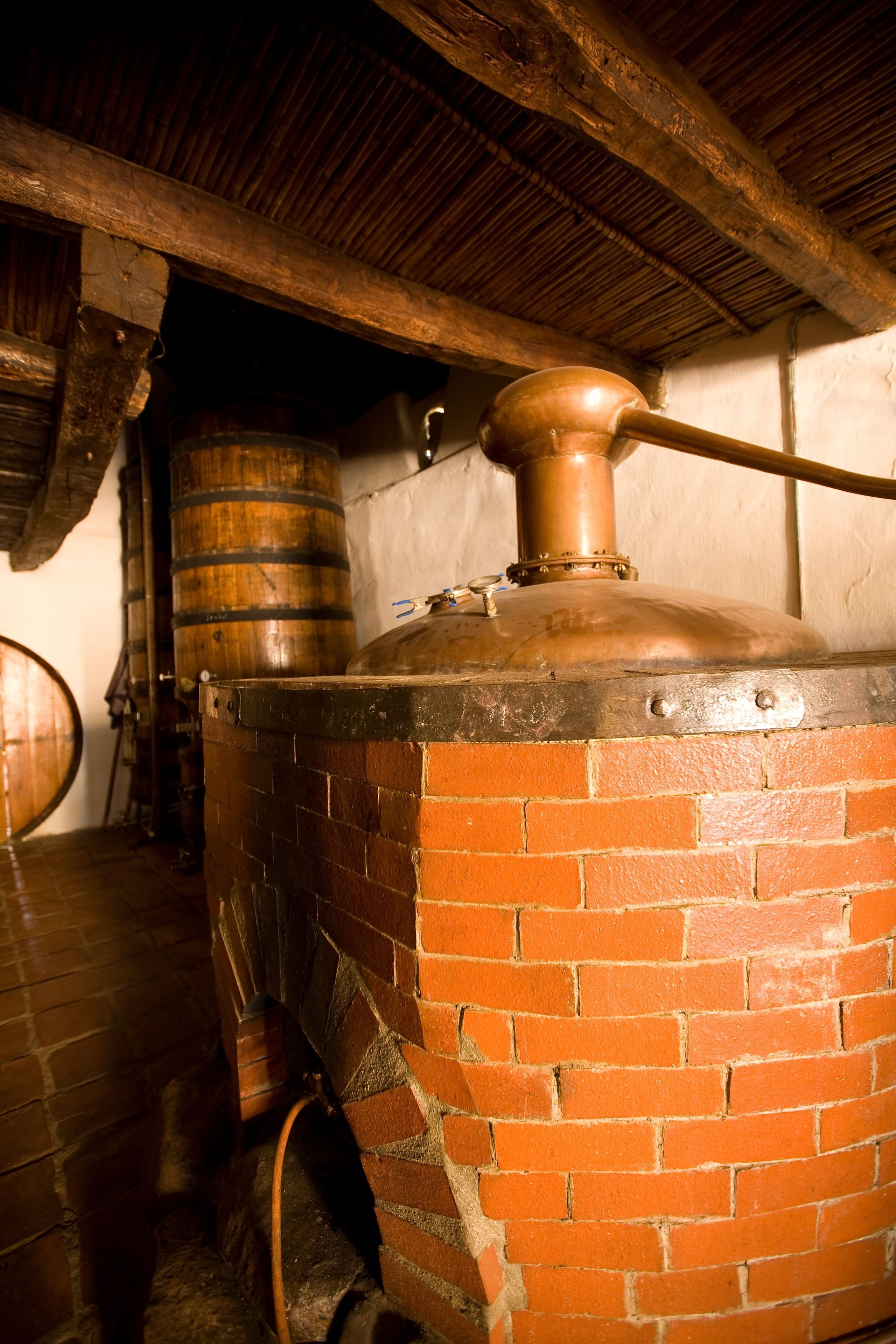 A brick oven with a copper pot on top, wooden barrels in the background, and a rustic wooden ceiling.