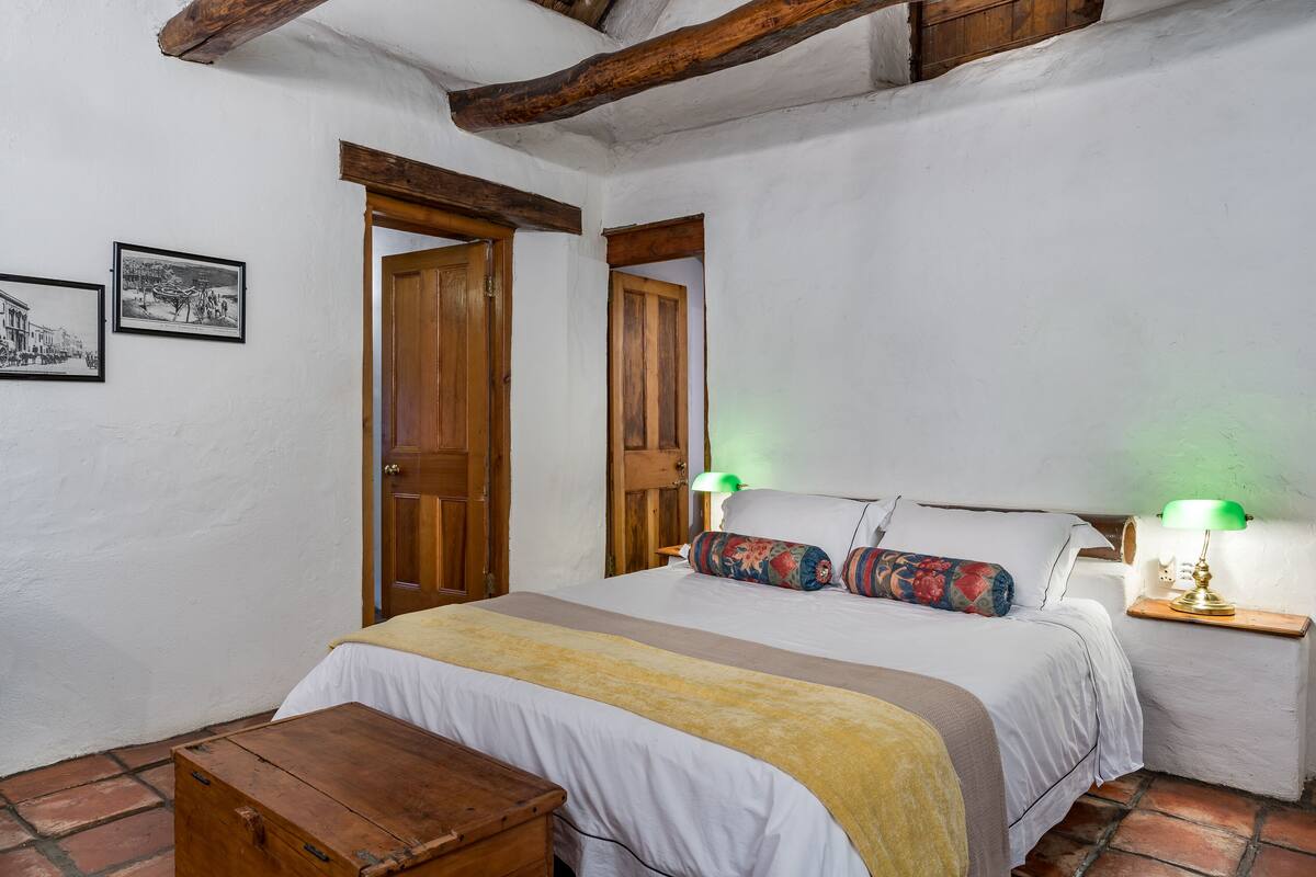 Un dormitorio con cama, mesitas de noche, un banco de madera y dos puertas.