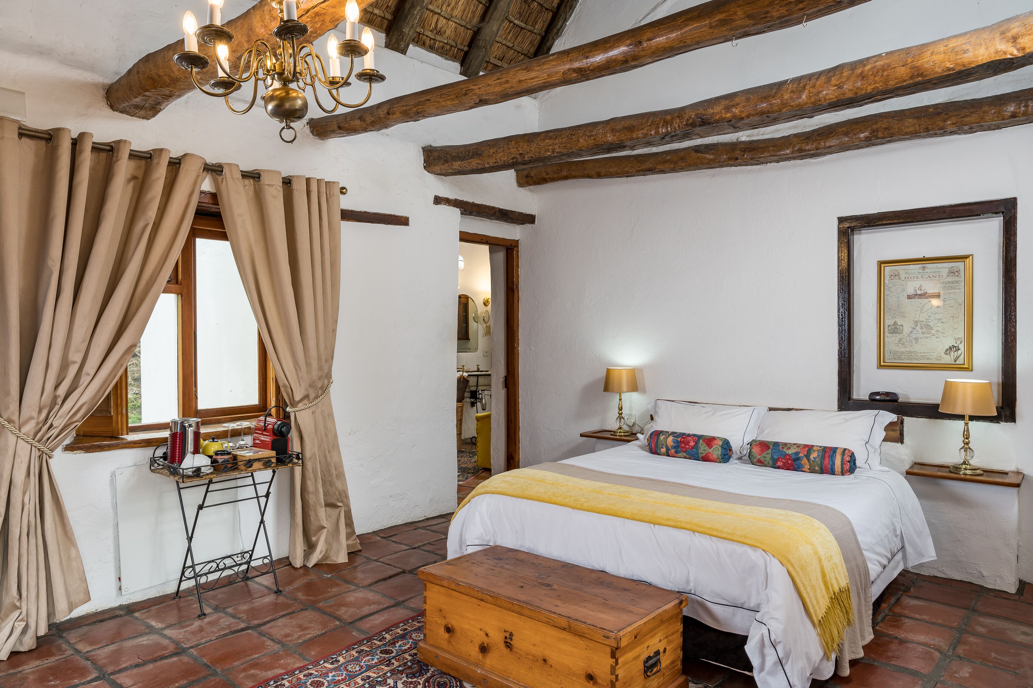 A traditional room with a bed, bedside lamps, a wooden chest, and a window with curtains.