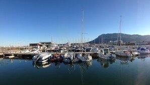 A marina with multiple boats docked, calm water, and a mountain in the background.