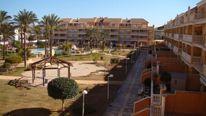 A resort with multiple-story buildings, a swimming pool, palm trees, and a playground.