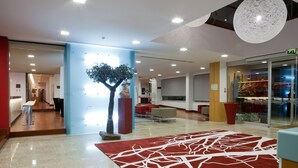 Un vestíbulo moderno con un tapete rojo y blanco, una escultura y un muro de vidrio.