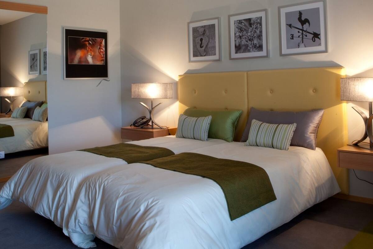 Ein Hotelzimmer mit einem großen Bett, zwei Nachttischen, einem Spiegel und drei gerahmten Bildern an der Wand.