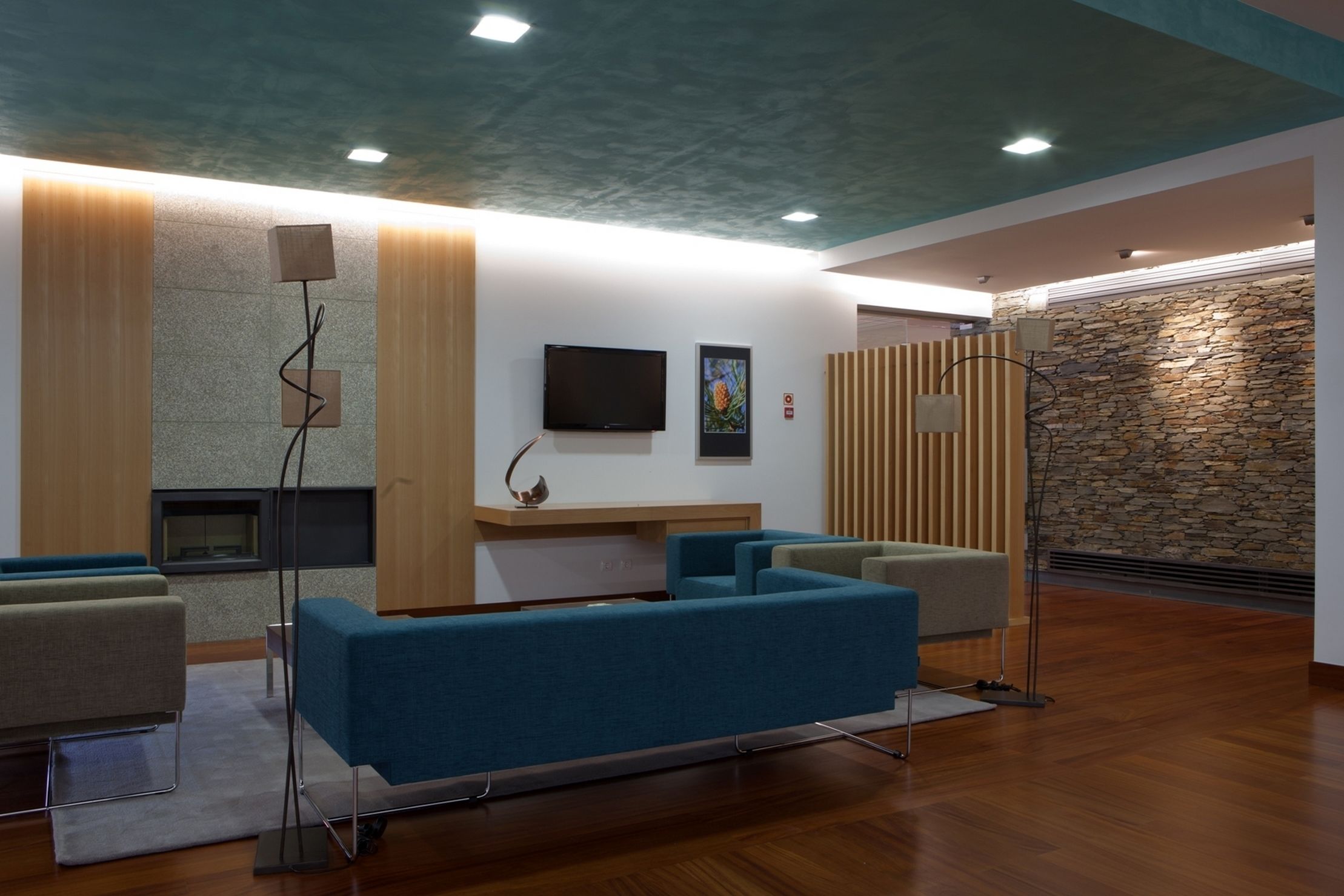 A modern reception area with a stone wall, blue sofas, a flat-screen TV, and a fireplace.