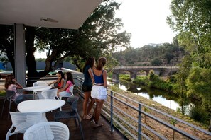 An outdoor patio with tables and chairs, overlooking a river and a bridge. - Hotel Santa Margarida (Oleiros)
