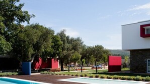 Zona de piscina con cubierta de madera, jacuzzi y edificio moderno con detalles en rojo.