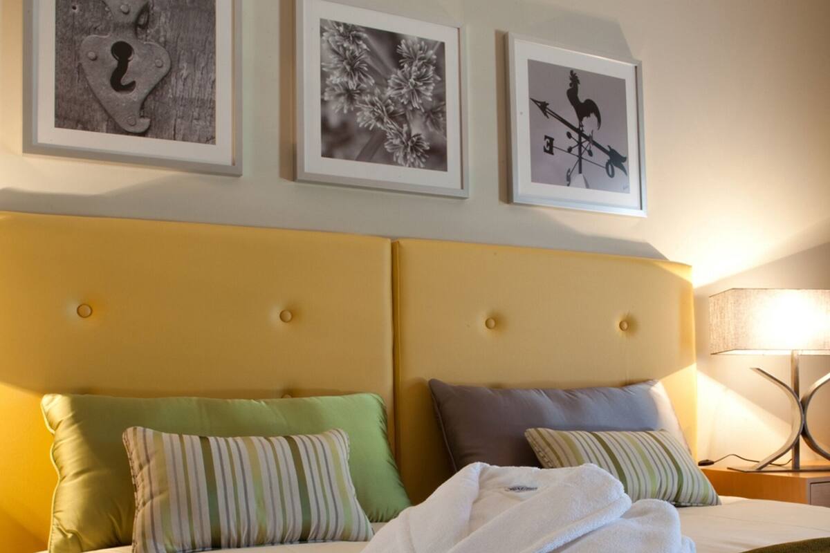 Ein Hotelzimmer mit einem Bett, Kissen, einem zusammengefalteten Bademantel und drei gerahmten Bildern an der Wand.