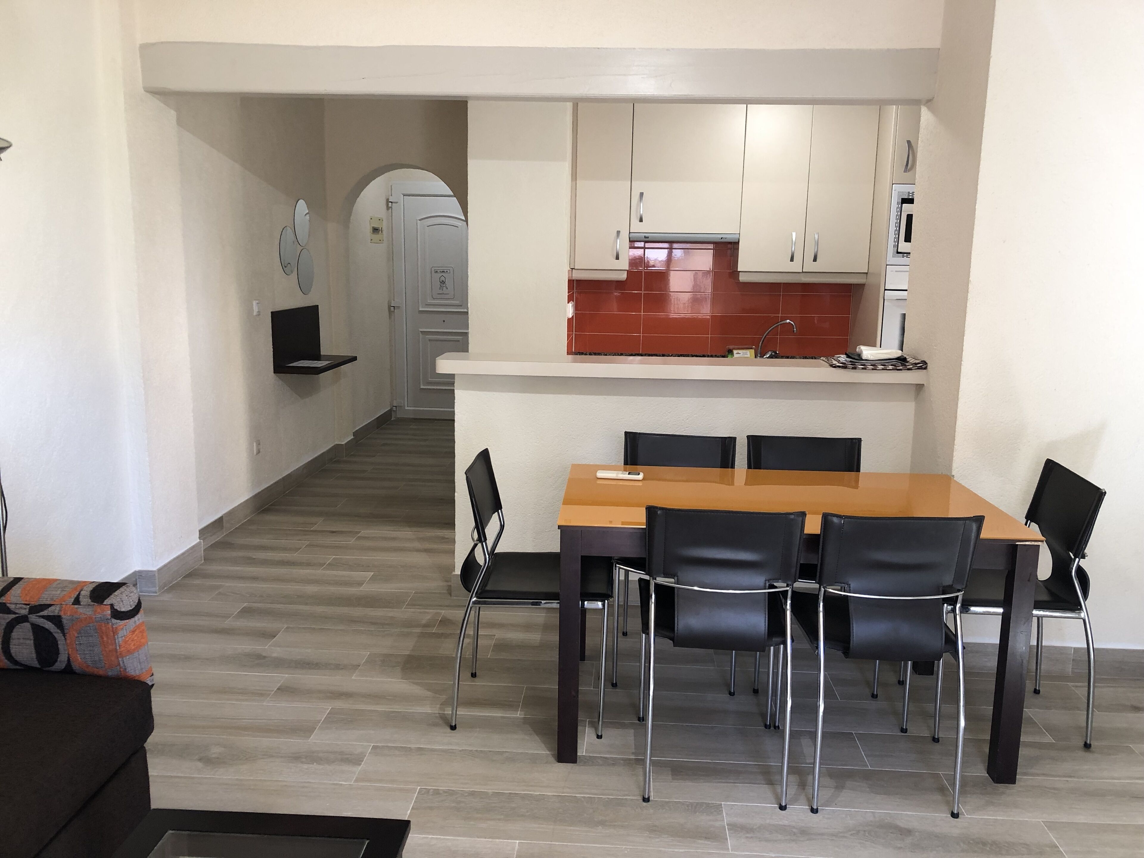 A compact kitchen with white cabinets, a red backsplash, and a dining area with a wooden table and black chairs.