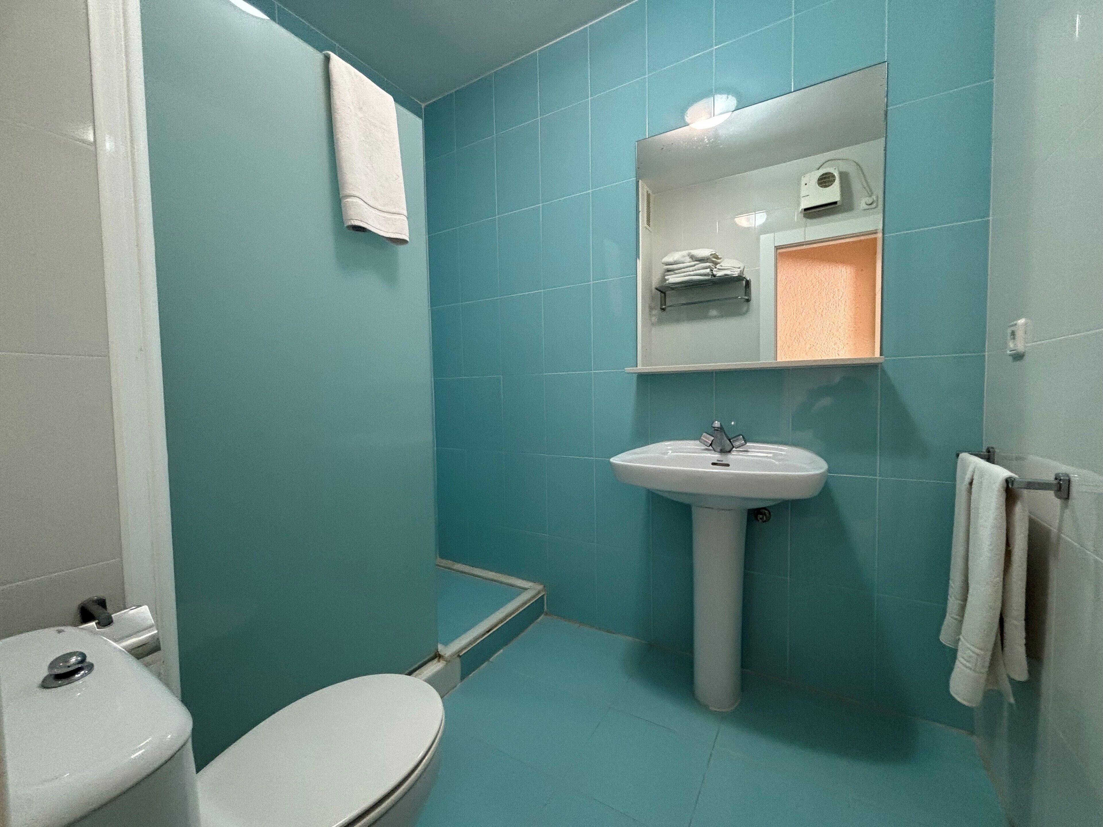 A bathroom with teal walls, a white sink, and a toilet.