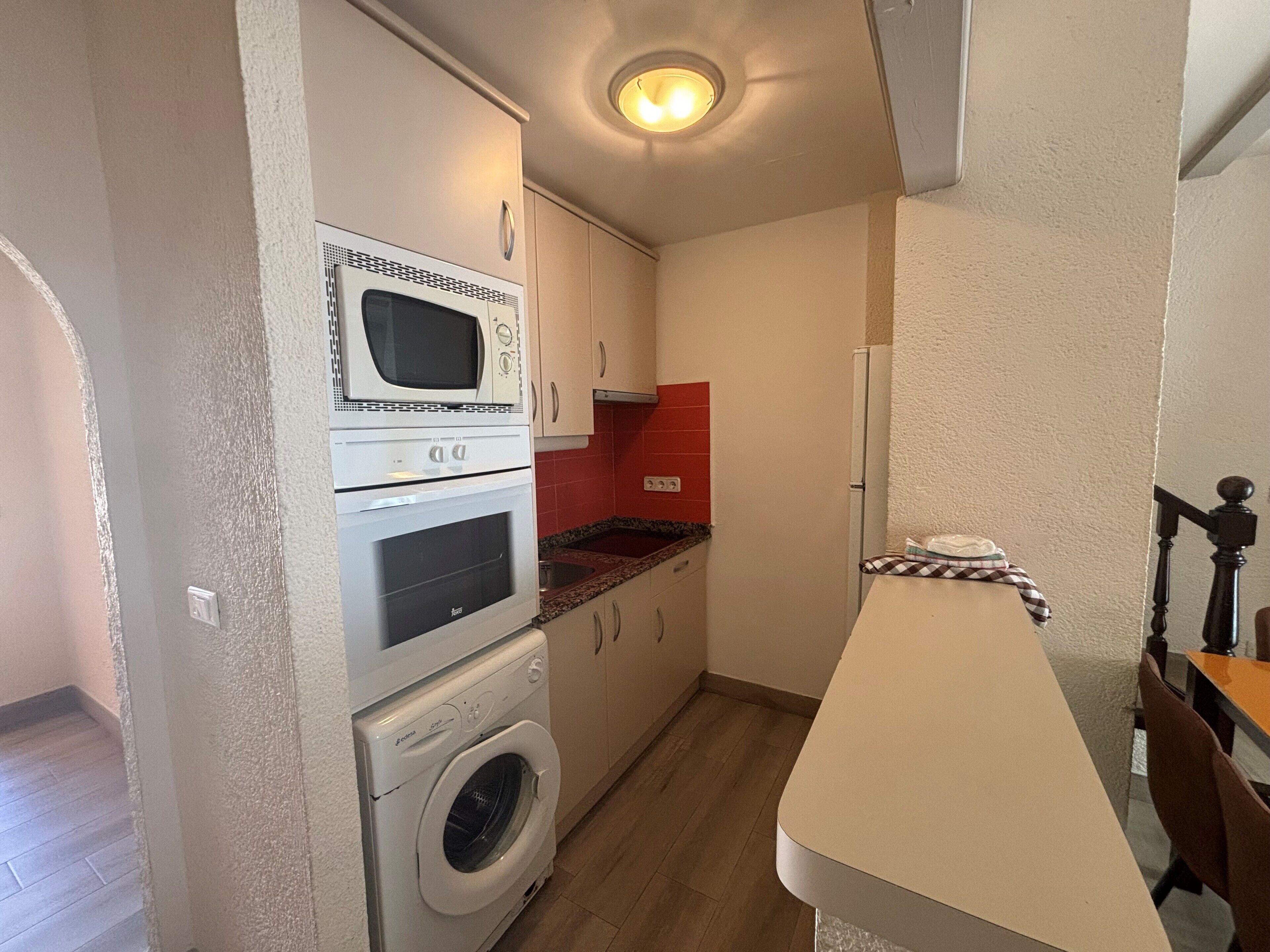 Een functionele keuken met een magnetron, oven en wasmachine.