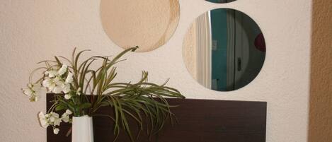 A white vase with flowers on a dark wooden shelf against a wall with three circular mirrors.