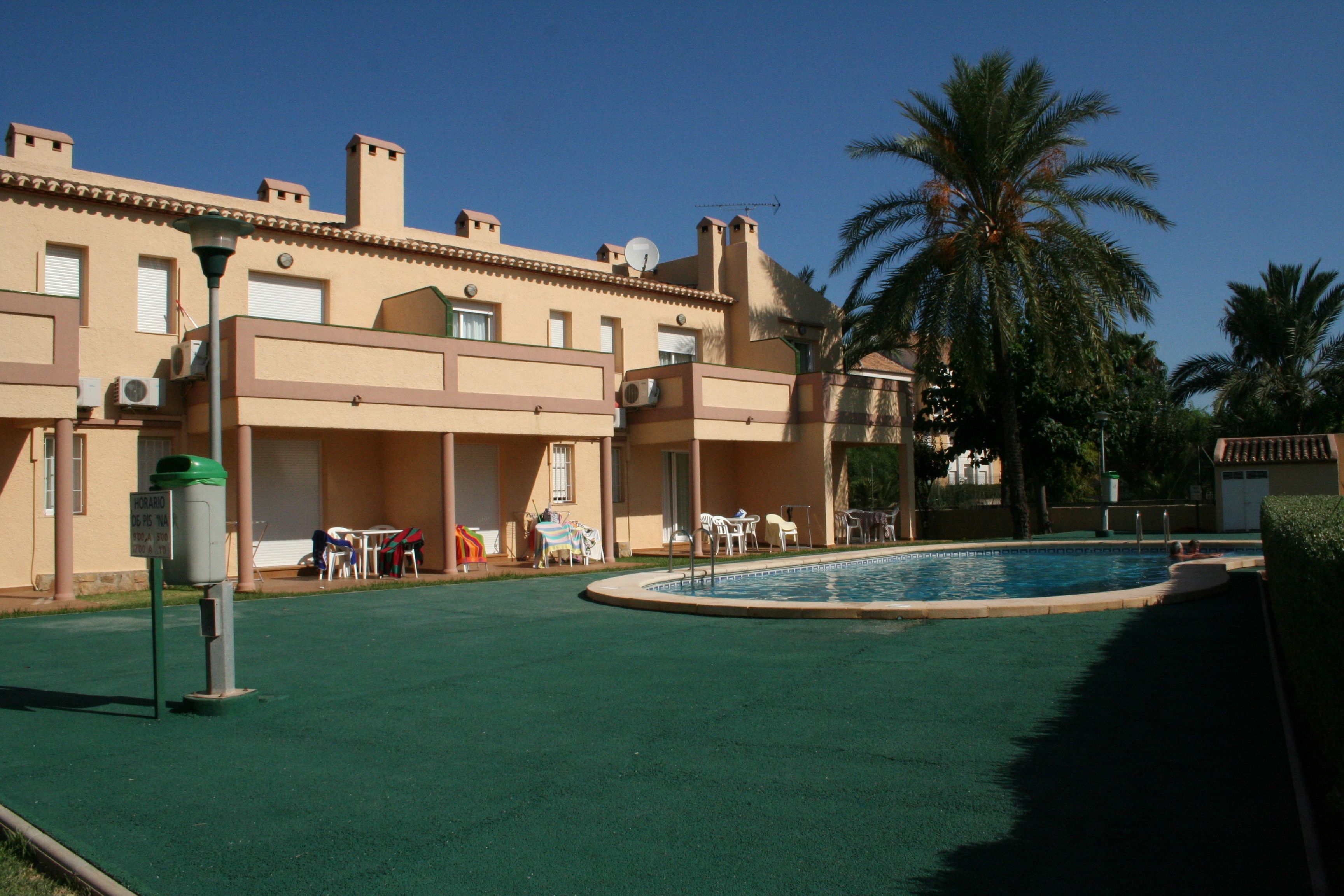 A pool area with a palm tree, outdoor seating, and a building with multiple windows and air conditioning units.