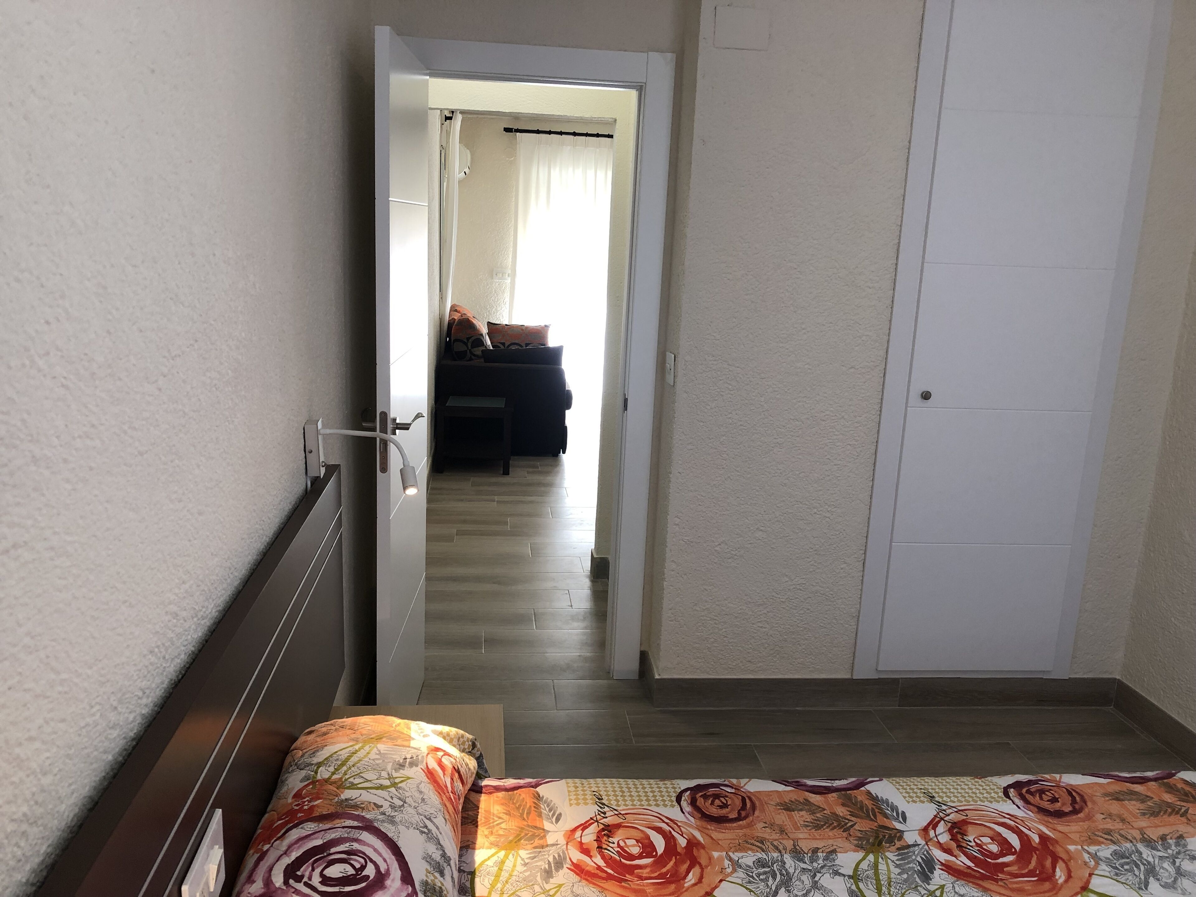 Un dormitorio con una cama, una puerta que da a una sala de estar y un armario blanco.