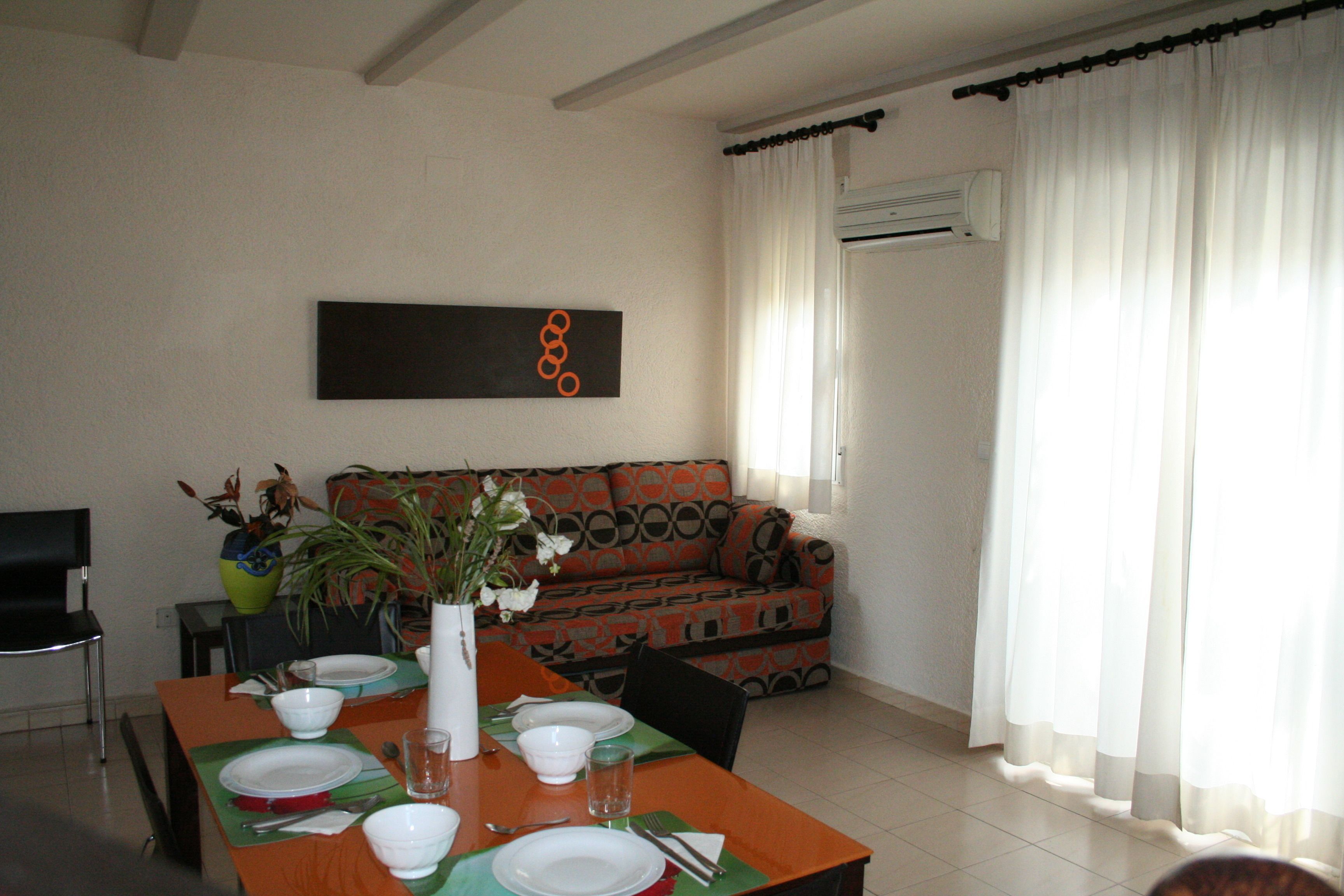 A dining area with a table set for four, a sofa, and a potted plant.