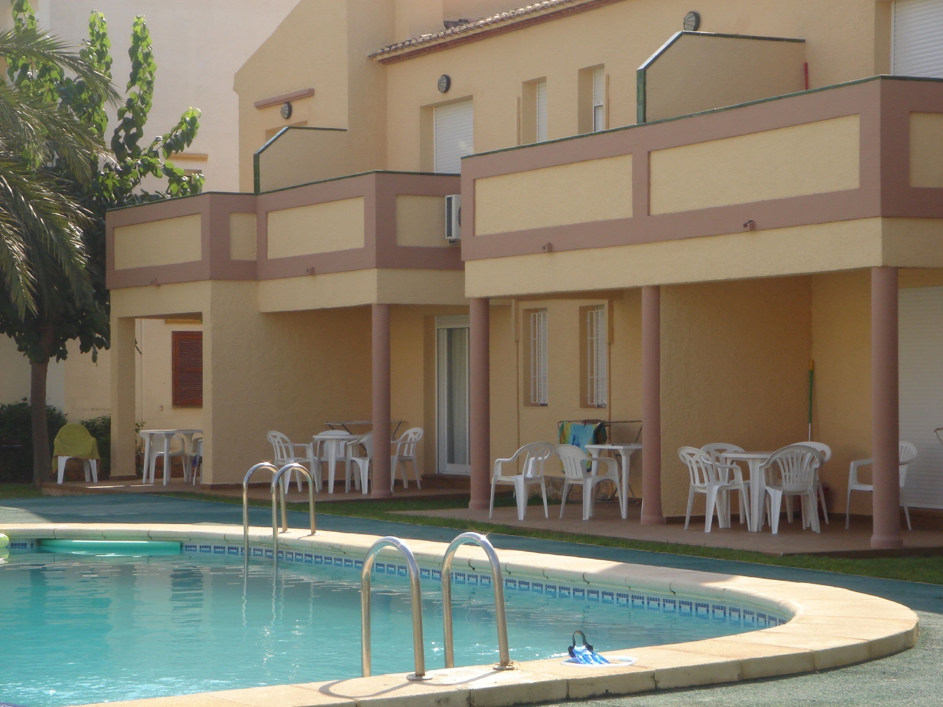 Un espace piscine comprenant une piscine, des chaises longues et un bâtiment doté d’un balcon.