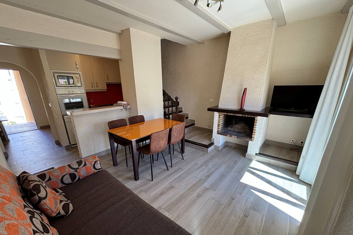 A modern living room with a dining area, a fireplace, and a kitchen in the background.