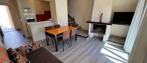 Una sala de estar moderna con comedor, chimenea y cocina al fondo.
