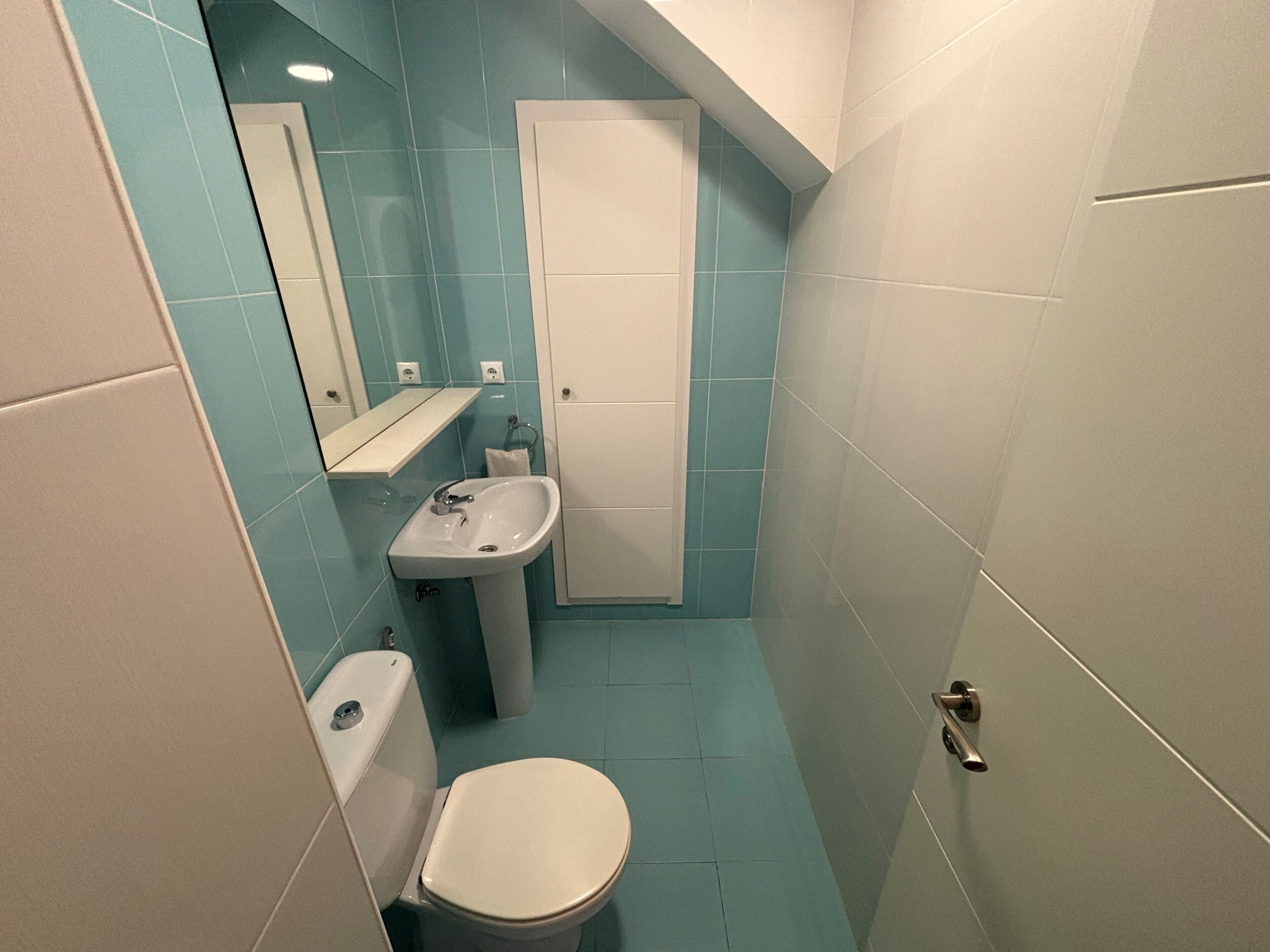 A small bathroom with a toilet, sink, and a mirror.