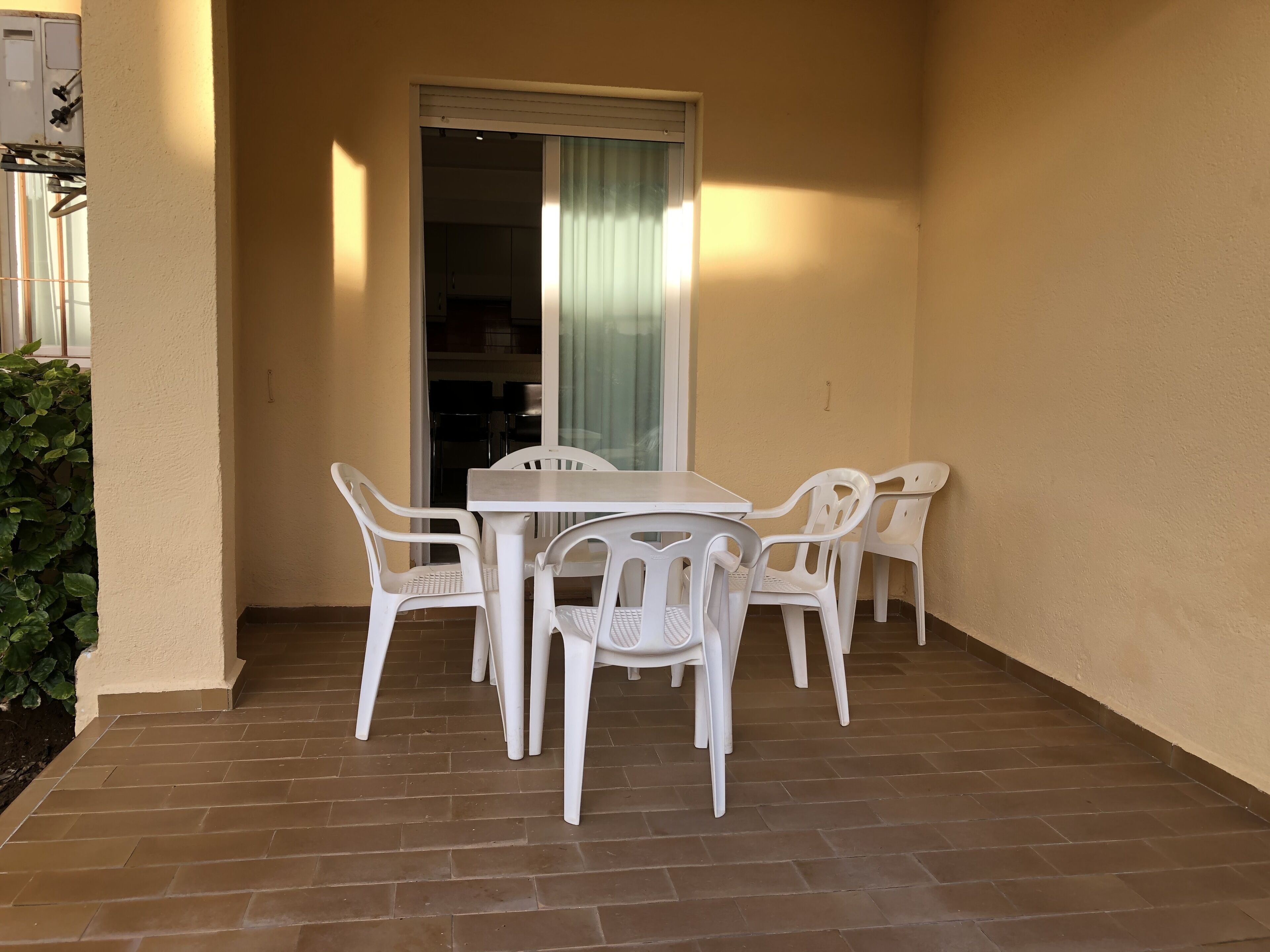 A small patio area with a white table and four chairs, a sliding glass door, and a brick floor.