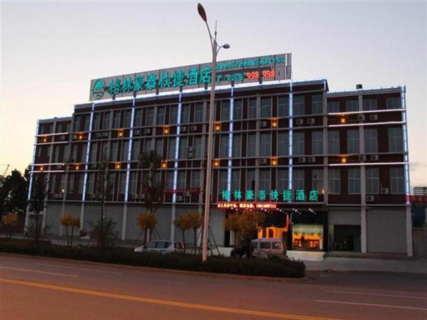 Un hotel de varios pisos con un letrero llamativo, una zona de estacionamiento y una farola.