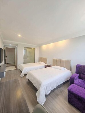 A hotel room with two beds, a desk, a purple chair, and a glass partition.