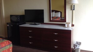 Habitación de hotel con televisión, cómoda, espejo, lámpara y cubo de basura.
