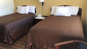 Habitación de hotel con dos camas individuales, una mesita de noche con lámpara y una silla.