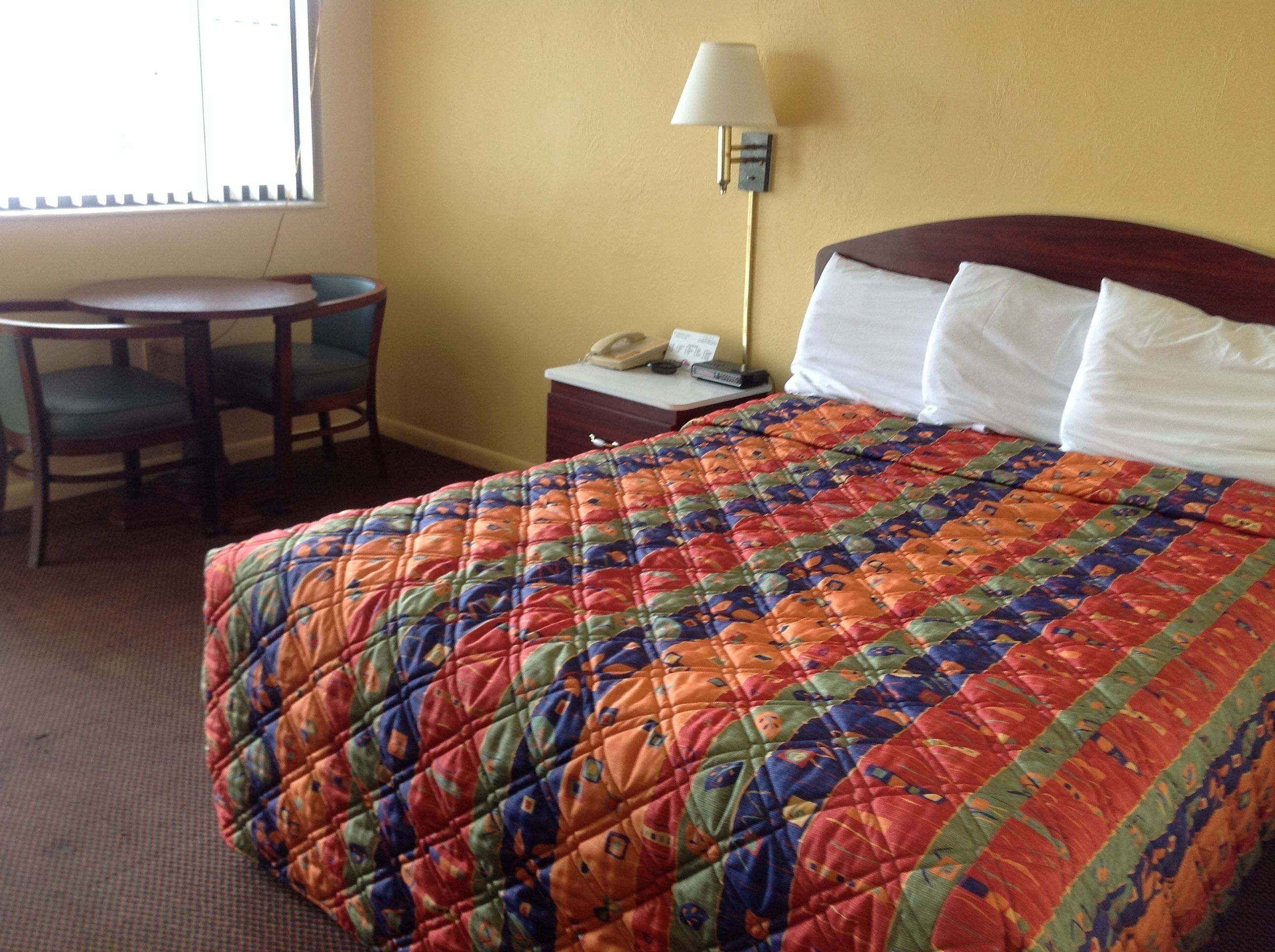 A hotel room with a bed, a desk, a chair, a lamp, and a telephone.