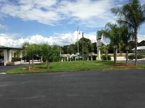 A parking lot with a few cars, surrounded by palm trees and a building with a green roof. - Economy Inn (Okeechobee)