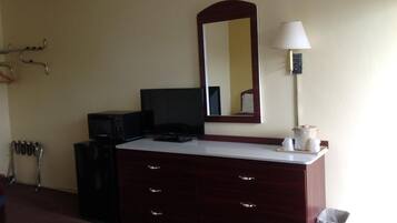 Habitación de hotel con tocador de madera oscura, televisor de pantalla plana, lámpara y espejo en la pared.