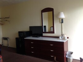 Habitación de hotel con tocador de madera oscura, televisor de pantalla plana, lámpara y espejo en la pared.
